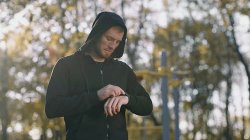 Young Man Checking Fitness Tracker While Jogging Outdoors in a Park