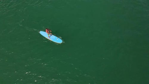 vertical down aerial drone bird's eye view of Caucasian man exercising on a sup paddle board in turq