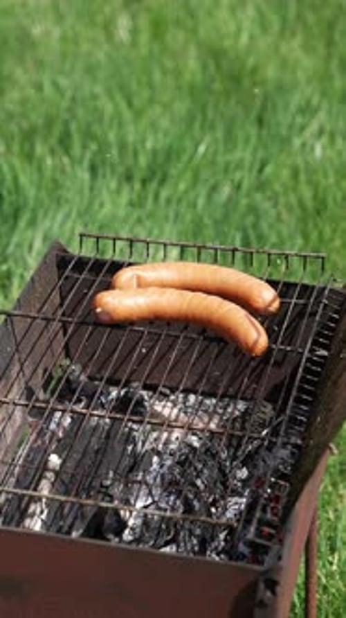 Man puts sausages into a grill for frying. Cooking hot dog sausages on fire. Barbecue in nature.