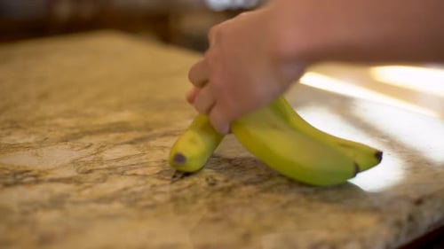 Hand Separating Banana from Bunch on Countertop