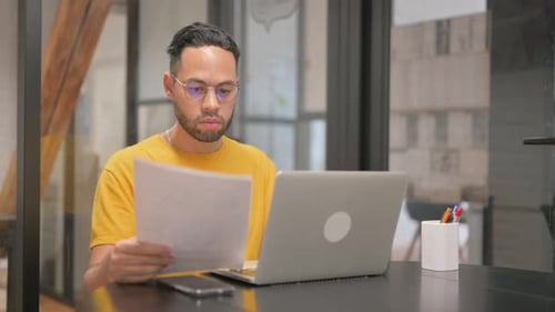 Young Adult Working with Laptop and Paperwork