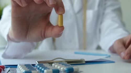 Doctor Showing Capsule Pill Sitting at Desk in Clinic