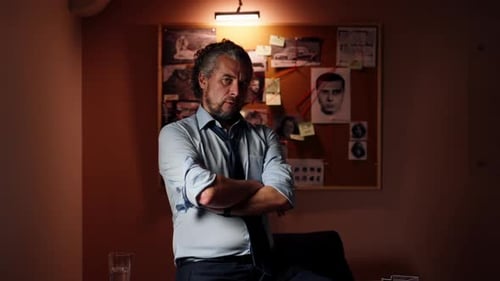 in the Detective's Office Middleaged Investigator in a Shirt and Tie Sits on a Table Looking at the