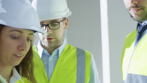 Team of Engineers in Hard Hats Having Conversation, Looking at Blueprint, inside Building Under Con