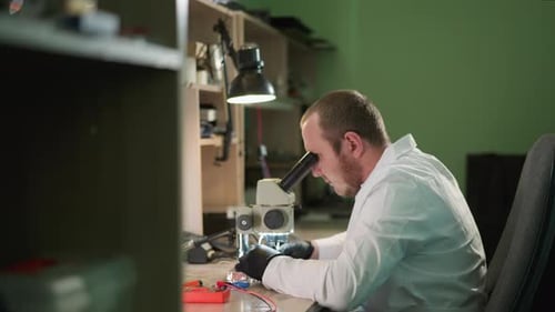 Man Examining Sample Through Microscope in Lab