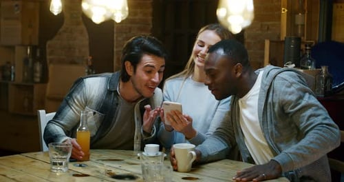 Slow motion of smiling friends having coffee at cafe and having fun with mobile cell phone. Shot i