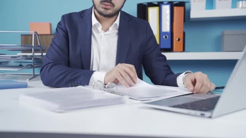 Man Works on Laptop and Organizes Files at Desk