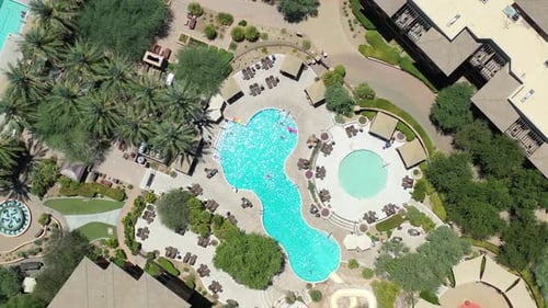 A drone lowers over a beautiful luxury destination pool as fellow travelers enjoy their vacation.
