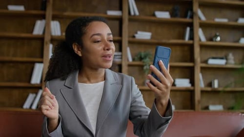 Excited Woman Video Calling on Phone in Library