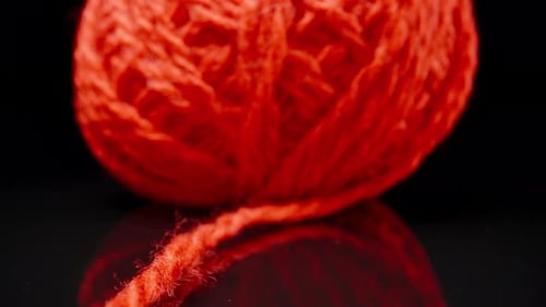 A ball of red woolen threads on black glass.. Dolly slider extreme close-up. Laowa Probe