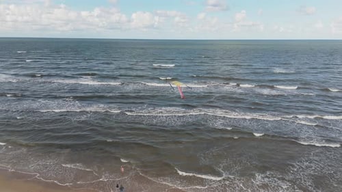 Epic drone shot of the colorful kite flying in the air with the Baltic Sea and a beach in the backgr