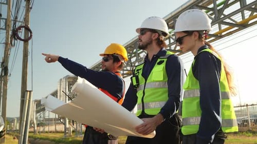 Workers discuss construction plans under a bridge at sunset in a construction site