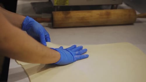 Flattening Dough With Hands Wearing Blue Gloves
