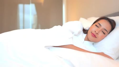 Beautiful Asian woman sleeping in comfortable bed with white linen, pillow and duvet. Tired lady tak
