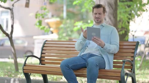 Frustrated Man Using Tablet on Park Bench