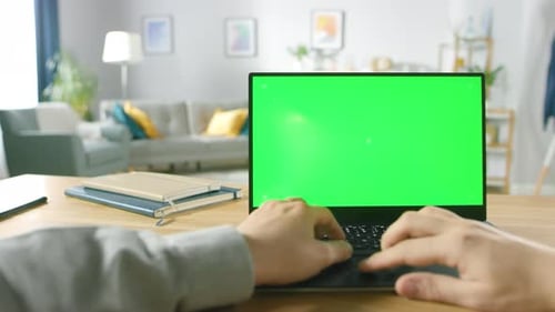 Professional Freelancer Works on a Laptop with Green Mock-up Screen while Sitting at the Desk in Hi