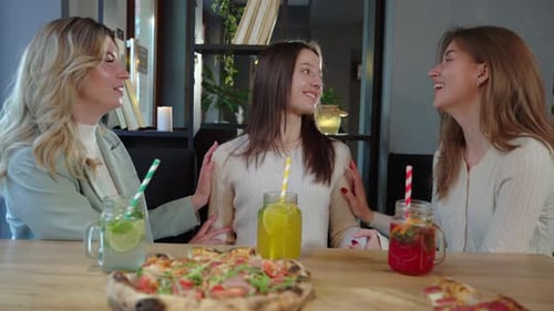 Lächelnde junge Freundinnen essen Pizza und Getränke im Restaurant