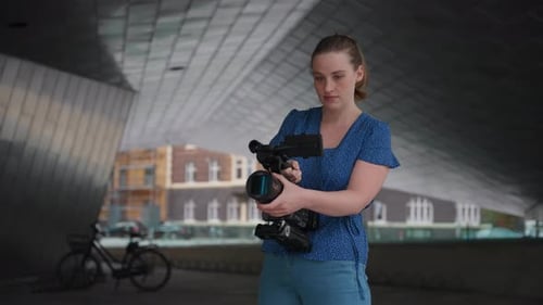 Young Woman Adjusts Video Camera in Urban Setting