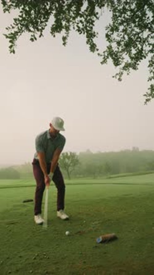 Male golfer hitting iron off tee with 3/4 swing on foggy morning