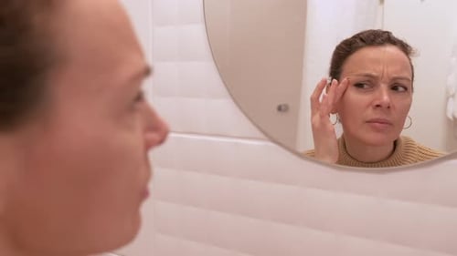 Woman Examines Face in Mirror in Bright Bathroom