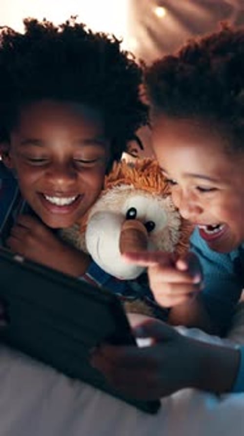 Two Children Looking at Tablet in Bed