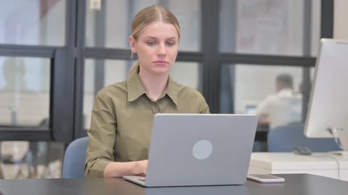 Woman working on laptop in office smiles at camera