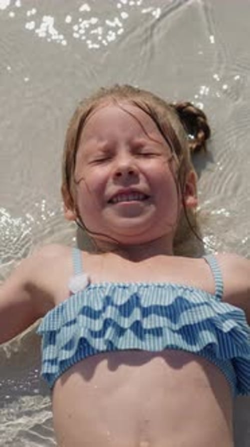 Little Girl in Swimsuit Waves Hands in Surfline on Beach