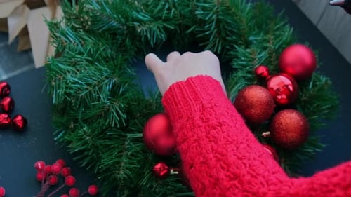 Hands Crafting a Christmas Wreath with Red Ornaments