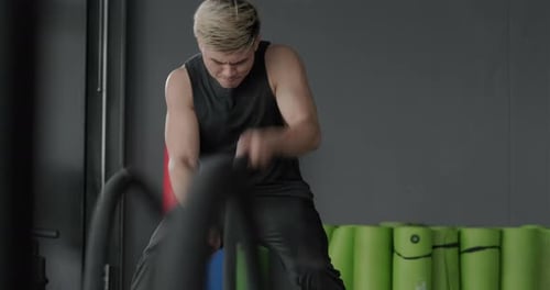 Young man battle ropes exercise in the fitness gym, Powerful guy using ropes during cross fit