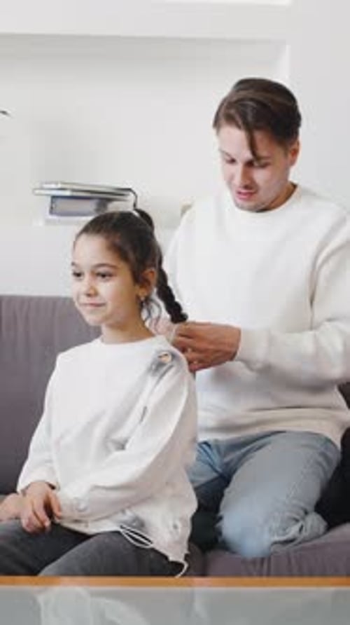 Dad Braids Daughter's Hair on Sofa in Living Room
