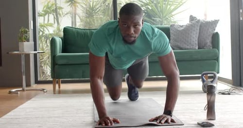 Exercising on yoga mat, African American man doing mountain climbers in living room, copy space