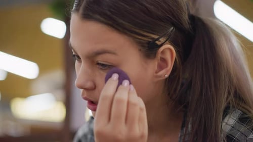 Closeup View of Young Lady Using Sponge to Blend Makeup on Face