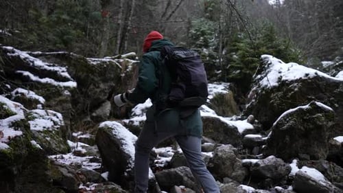 Backpacker With Camera Hiking On Rocky Mountain During Snowfall In Winter. tracking shot