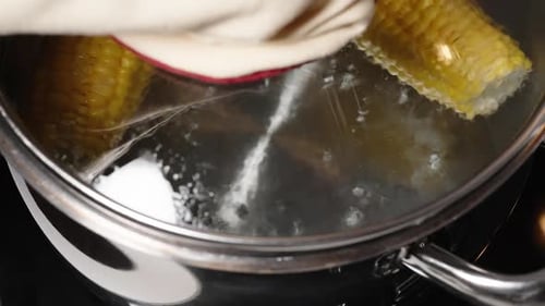 Two boiled corn cobs are simmering in a pot as I lift the lid. The camera moves in a dolly motion.