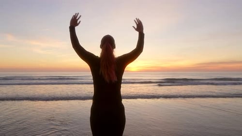 Frau breitet ihre Arme aus und beobachtet den Sonnenaufgang, während sie bei Sonnenaufgang atmet