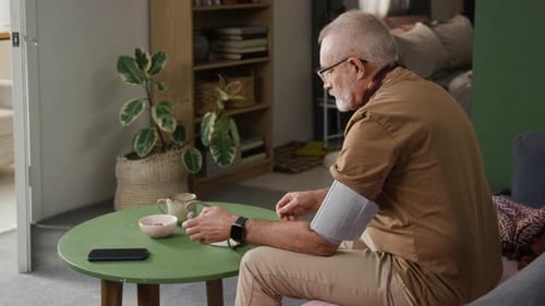 Senior Man Checking Blood Pressure Using Digital Device at Green Round Table