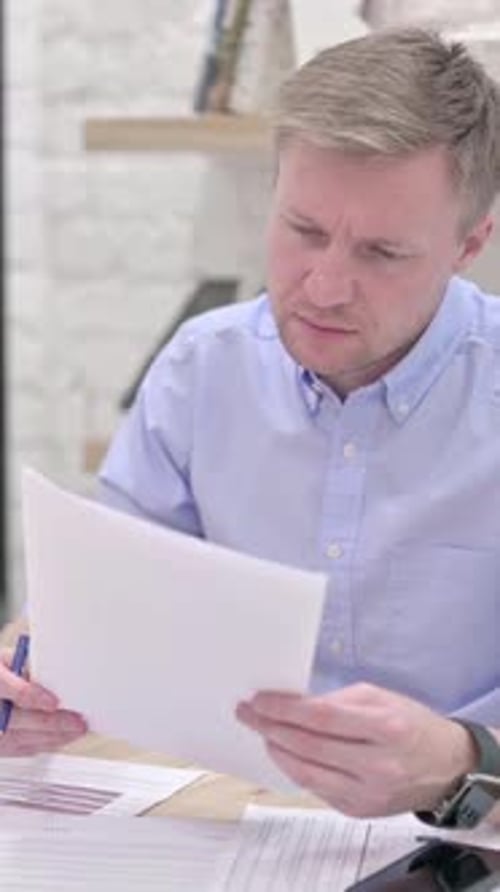 Man Reviews Documents at Desk in Bright Room