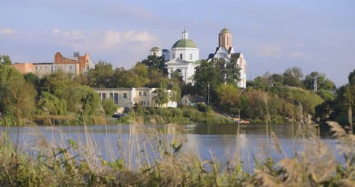 A peaceful riverside scene with lush greenery, a bridge, and historic buildings