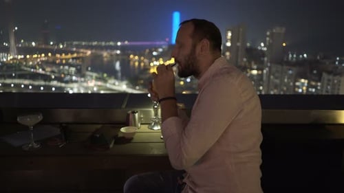 Young Man Relaxing and Drinking Cocktail Sitting on Terrace in Bar At
