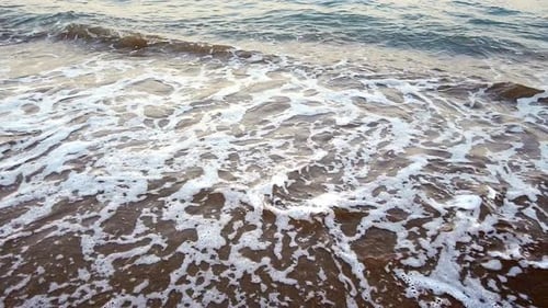 Sea Waves Wash the Dark Sand of the Beach Line at Sunset