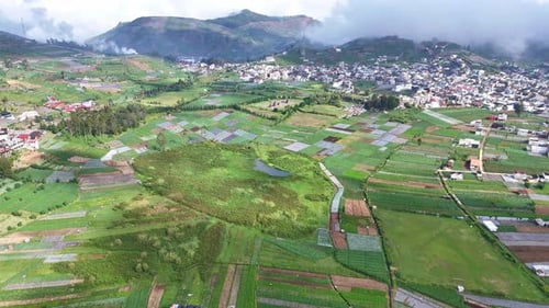 Aerial view of a small town surrounded by farmland and lush hills with scattered clouds