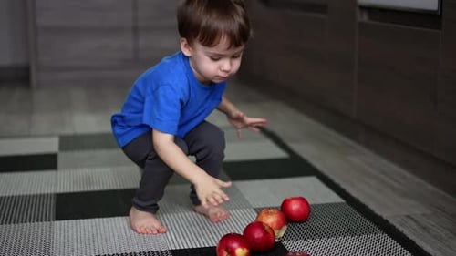 Cute Child Plays with Red Apples in Kitchen