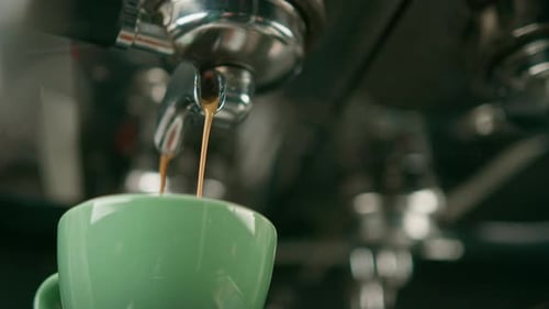 Pouring coffee flows from the machine into the cup making hot drink using the filter holder freshly