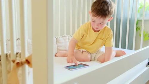 Young Child Interacts With Smartphone in Crib