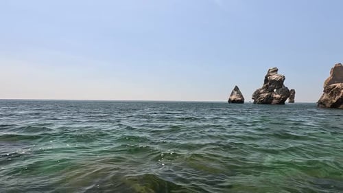 Sea Water Surface Camera Flies Over the Calm Azure Sea with Volcanic Rocky Shores on Background