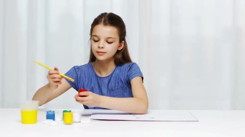 Girl painting with brush at white desk indoors