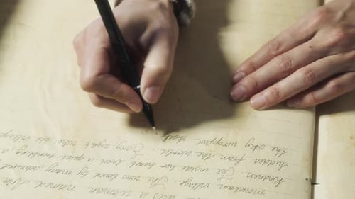 Close-up of hands writing in an old notebook under warm natural light.