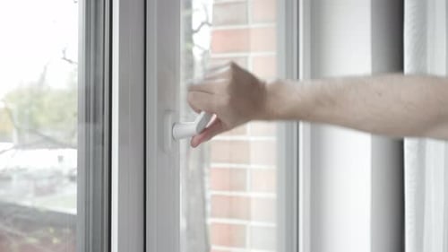 A man closes the frame of a slightly ajar PVC plastic window with his hand.