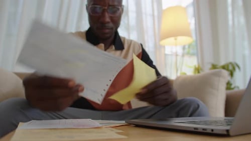 Adult Reviews Documents at Home with Laptop