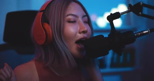 Woman with Headphones Singing into Microphone in Blue Light